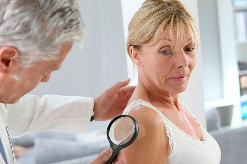 a doctor examines a papilloma on the arm